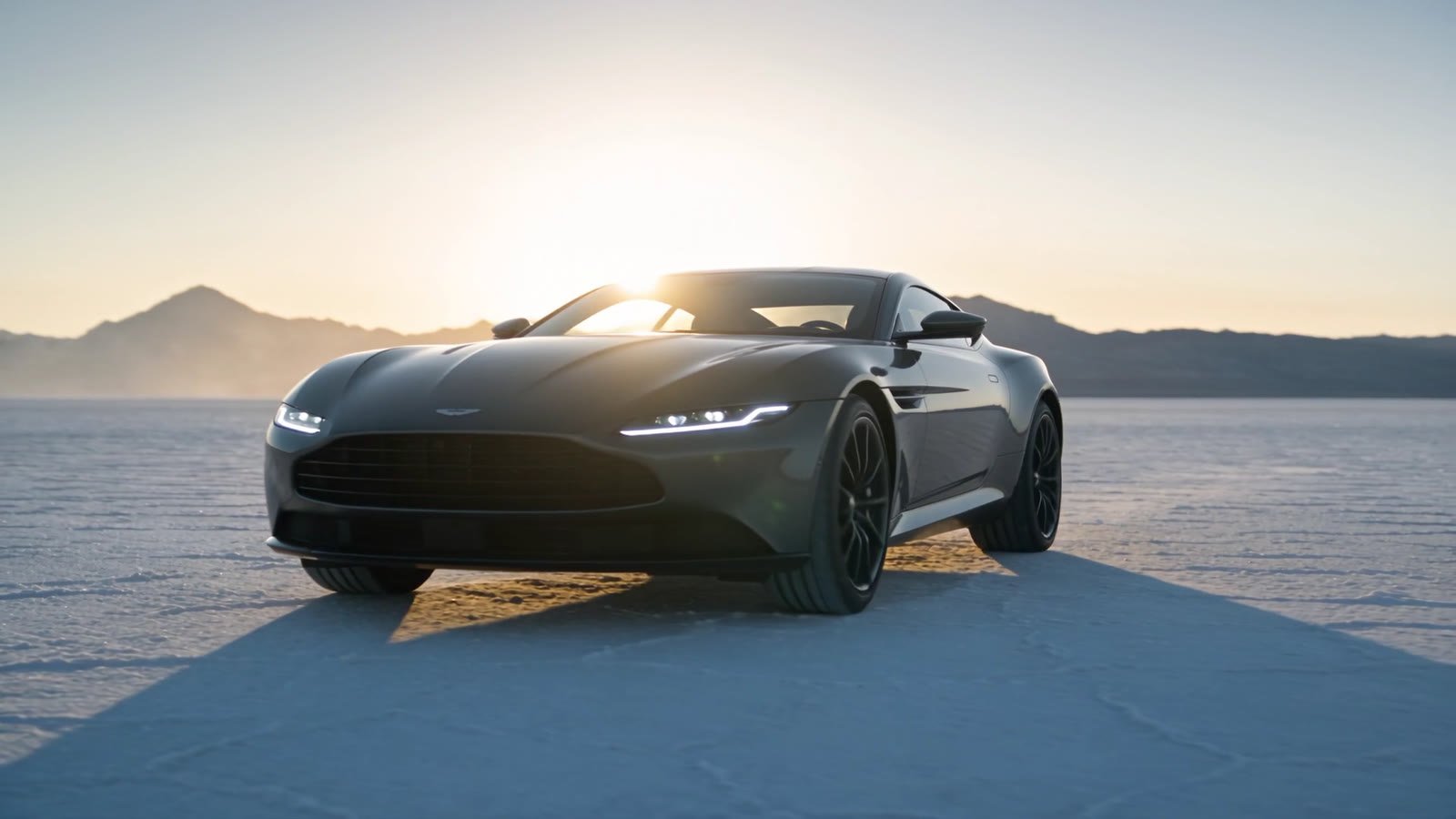 A grey sports car on a salt flat at sunset